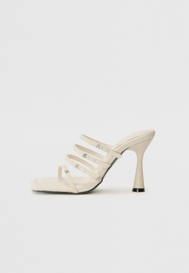 Sandales à talons hauts crème avec quatre fines lanières, bout carré, matériau texturé et un talon évasé avec un accent noir.