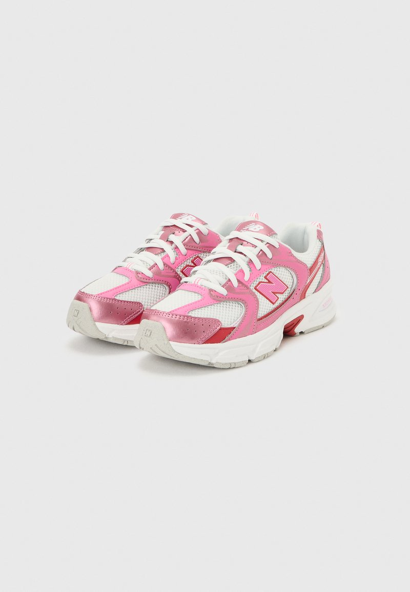 Paire de baskets de sport blanches et roses avec des superpositions en mesh et en synthétique, des lacets blancs et un logo "N" rouge sur les côtés.
