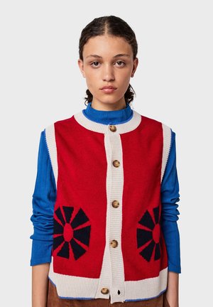 Rode gebreide vest met marineblauwe bloemenpatronen, crèmekleurige afwerking, knoopsluiting aan de voorkant, en een effen blauwe langearmige shirt eronder.