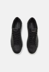 Baskets en cuir noir avec lacets plats, bout rond et semelle en caoutchouc blanche. Présente un logo sur la languette et sur le côté. Texture lisse.