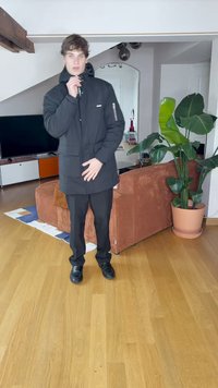 Čierny zateplený parka s vysokým golierom a predným zipsom, s bočnými vreckami. Čierne nohavice a topánky dokončujú vzhľad.