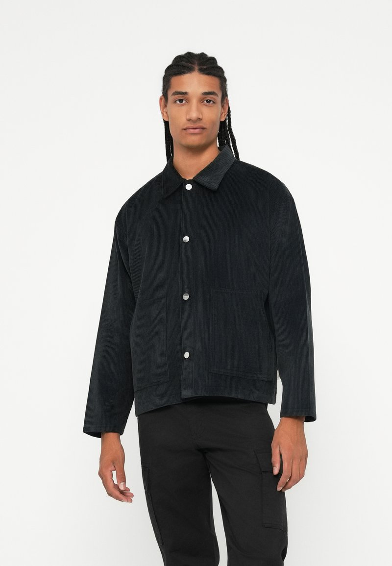 Sort corduroyjakke med krave, frontknapper i snap og to sidelommer. Designet har lange ærmer og en cropped pasform.