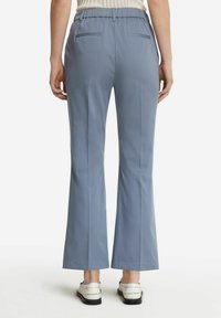 Ljusblå, utsvängda byxor i ett slätt, texturerat tyg. Har en hög midja och två bakfickor för diskret funktionalitet.