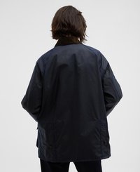 Casaco impermeável azul-marinho com colarinho em veludo-de-cotele, ajuste oversized e detalhes em botões de pressão, apresentando uma textura suave e mate.
