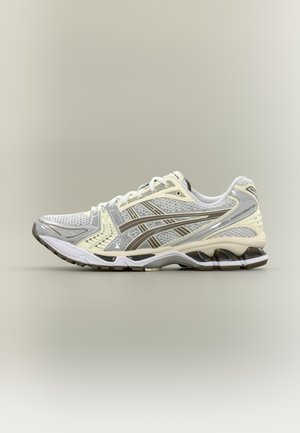 Laufschuh in Grau und Creme mit Mesh-Obermaterial, weißen Schnürsenkeln und gepolsterter Sohle mit markantem Wellenmuster und braunen Akzenten.