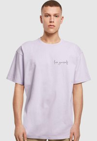 Lys lavendel bomulds t-shirt med korte ærmer. "Elsk dig selv" trykt i en kursiv grå skrifttype på venstre brystområde. Klassisk rund halsudskæring.