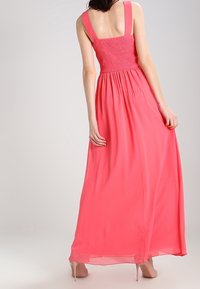 Abito maxi di un vivace rosa, con un corpo arricciato, spalline larghe e tessuto fluido che scende fino a terra. Texture liscia e leggera.