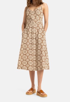 Brown midi dress with a white floral pattern, adjustable spaghetti straps, and side pockets; paired with tan platform sandals.