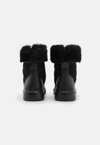 Bottes courtes en daim noir avec un revers en fausse fourrure, dotées d'une semelle en caoutchouc noire et d'un contraste texturé lisse sur le talon.