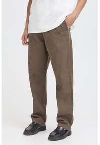 Pantaloni marroni in tessuto strutturato, caratterizzati da una vestibilità ampia, tasche laterali e taglio a gamba dritta. Abbinati a scarpe nere.