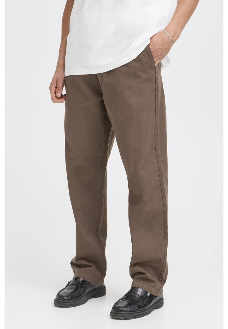 Pantaloni marroni in tessuto strutturato, caratterizzati da una vestibilità ampia, tasche laterali e taglio a gamba dritta. Abbinati a scarpe nere.