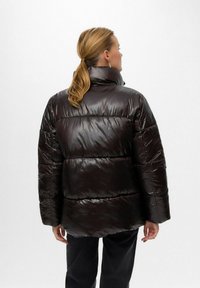 Särav must puffer-jakk kõrge kraega, millel on tikitud osad, pikad varrukad ja mugav lõige. Sile tekstuur, nähtavat riistvara ei ole.