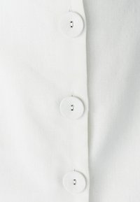 Biely textil so štruktúrovaným povrchom, ktorý má pozdĺž švu tri okrúhle gombíky. Gombíky sú biele s designom s prievlaky a malými otvormi.