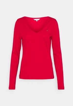 Czerwona koszulka z długim rękawem i dekoltem w serek z małym logo Tommy Hilfiger na piersi, pokazana na białym tle.