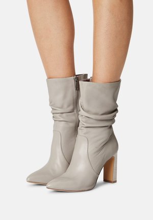 Bottes chevilles en cuir gris avec un design froncé, bout pointu et un talon carré. Fermeture éclair à l'arrière. Texture lisse et style minimaliste.