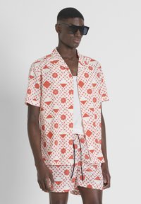 Korte mouwen shirt en shorts set in een wit en rood geometrisch patroon. Gemaakt van lichte stof, met een ontspannen pasvorm en een kraag.