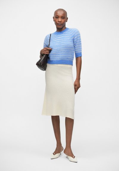 Pull en tricot rayé bleu clair à manches courtes, jupe midi crème à côtes, chaussures blanches à bout pointu et sac à main tissé noir.