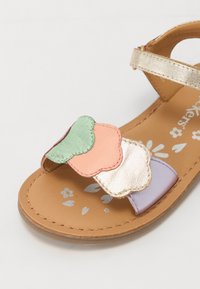 Bruine sandaal met decoratieve geschulpte lagen in mintgroen, perzikkleur, goud en lavendel op de band, met een bloemenpatroon op de inlegzool.