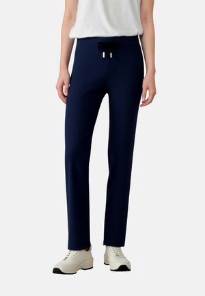 Navy blue jogger pants with an elastic waistband and drawstring, featuring a smooth texture and a tapered fit, paired with white sneakers.