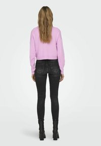Pull court rose avec des poignets côtelés associé à un jean skinny noir et des bottines à talons. La tenue présente un design ajusté.