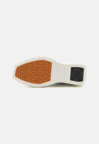 Semelle de sneaker blanche avec des motifs texturés en caoutchouc marron et des accents en caoutchouc noir. Présente un design de semelle géométrique pour une meilleure adhérence.