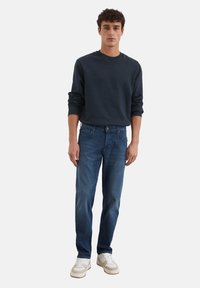 Felpa blu scuro abbinata a jeans azzurri chiari. I jeans presentano un design tradizionale a cinque tasche. Tessuto morbido con leggera scoloritura e vestibilità ampia.