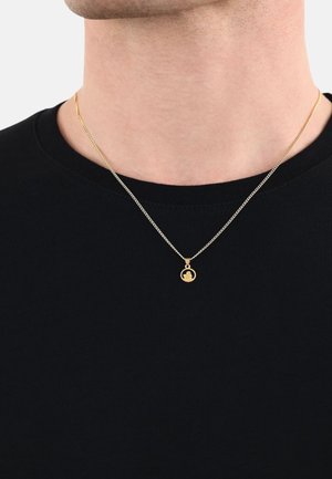 Collana con pendente d'oro su una catena sottile, con un ciondolo circolare dal design dettagliato, indossata sopra una maglietta nera.
