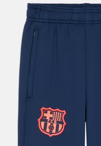 Pantalons de sport navy avec une taille élastique, ornés d'un écusson FC Barcelone brodé en orange et de poches latérales. Texture lisse.