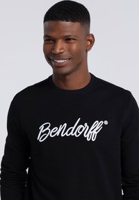 Black long-sleeve shirt made of soft fabric featuring a large white embroidered text "Bendorf" on the chest. Simple, fitted design.