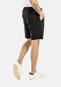 Pantalones cortos negros de corte relajado, fabricados en algodón, con bolsillos laterales y traseros, y una cintura elástica. Con un discreto logotipo.