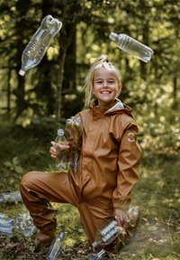 Bruin waterdicht pak met een lichtgrijze capuchon, met een gestructureerde afwerking, omgeven door plastic flessen in een bosrijke omgeving.