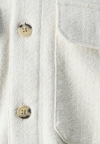 Licht beige overhemd met knopen, gemaakt van gebroken stof, met twee knopen en een borstzak met een klep.