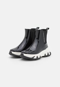 Botas de lluvia negras brillantes hasta el tobillo con suelas blancas gruesas y tiradores, que cuentan con paneles laterales elásticos y el texto "LEMON JELLY RAINWEAR".