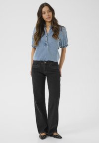 Camisa de mezclilla de color azul claro con tapeta de botones y mangas con vuelta, combinada con unos pantalones vaqueros anchos de tiro alto en color negro y unos zapatos planos negros.