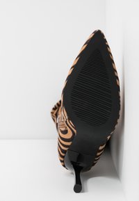 Zapato de tacón alto con punta afilada en ante a rayas en tonos marrón y negro, con suela de goma negra. Presenta un tacón de aguja delgado y un fondo texturizado para mayor agarre.
