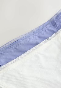 Gros plan sur des bandes de lingerie en tissu côtelé lavande et blanc avec un délicat bord de dentelle sur un fond clair.