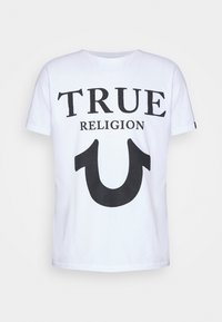 Vit bomulls t-shirt med kraftig svart text som säger "TRUE RELIGION" och en stor svart hästsko-logotyp på framsidan. Korta ärmar.