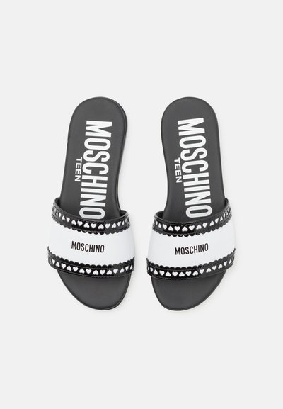 Sandales à glissière noir et blanc avec une large bride ornée de découpes en forme de cœur, affichant un logo "MOSCHINO" en lettres audacieuses et une finition lisse.