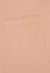 Svetloružová rebrová pletenina s malou štvorcovou vreckom, na hornom pravom rohu s žltým vyšitým textom "Blkviis".