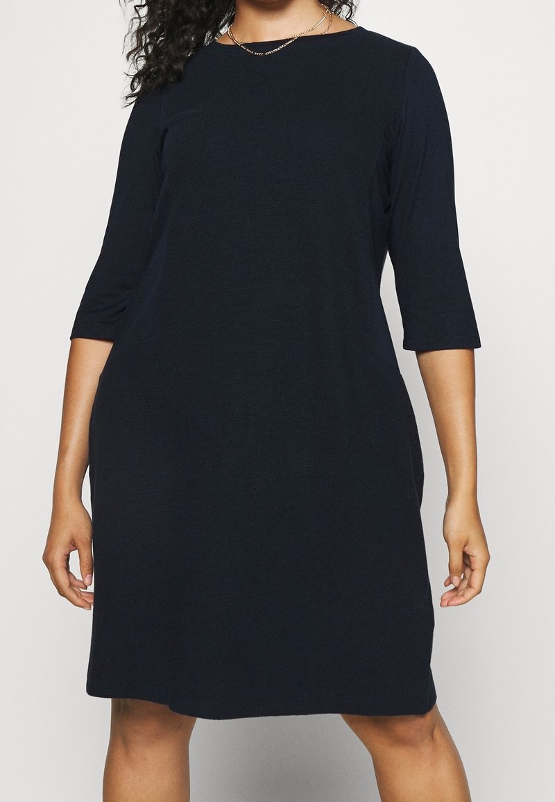 Marinblå knälång klänning med trekvartsärmar, rund halsringning, mjuk textur och en avslappnad passform. Inga synliga mönster eller detaljer.