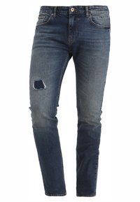 Mörkblå slim-fit denimjeans med en liten lapp och slitage på övre vänstra låret.