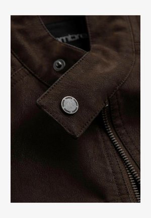 Brązowa skórzana kurtka o teksturowanej powierzchni, z metalowym zatrzaskiem i zamkiem błyskawicznym z przodu. Logo marki jest widoczne na guziku.