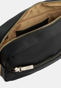 Borsa in tessuto nero con zip dorata, caratterizzata da un'esterno liscio, foderata in beige all'interno e con una tasca aggiuntiva interna. Design compatto.