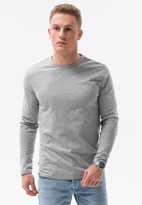 Graues Langarm-T-Shirt aus Baumwolle, mit Rundhalsausschnitt und regulärer Passform, kombiniert mit hellblauen Jeans und einer silbernen Uhr.