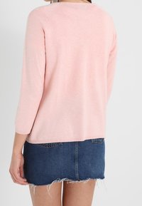 Ljuspink knitted tröja med trekvartsärmar, kombinerad med en denimkjol med fransad fåll och bakfickor.