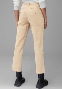 Beige corduroybroeken met een rechte pijp, voorzien van twee achterzakken en metalen knoopaccenten, gecombineerd met zwarte enkelboots.