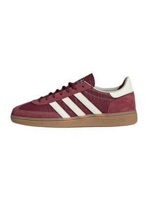 Zapatilla baja Adidas en burdeos con tres rayas blancas, lengüeta blanca en el talón y suela de goma beige, vista lateral sobre fondo blanco.