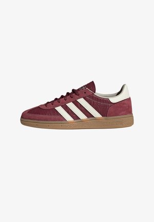 Baskets basses Adidas couleur bordeaux avec trois bandes blanches, languette de talon blanche et semelle en gomme naturelle, vue de côté sur fond blanc.