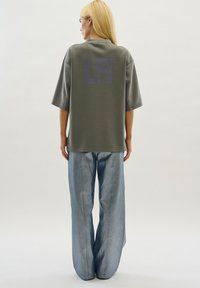 Losse, grijze polo met een gestructureerde stof en een grote donkergrijze "L9"-afbeelding op de rug, gecombineerd met glanzende, lichtblauwe wijde broek.