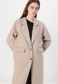 Beige, villasekoitus takki, jossa on lovettu kaulus, kaksi etutaskua ja kaksi nappia. Ominaisuuksiin kuuluu rento istuvuus ja pehmeä rakenne.